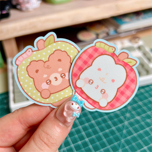 Two cute animal stickers held by a hand on a green cutting mat.