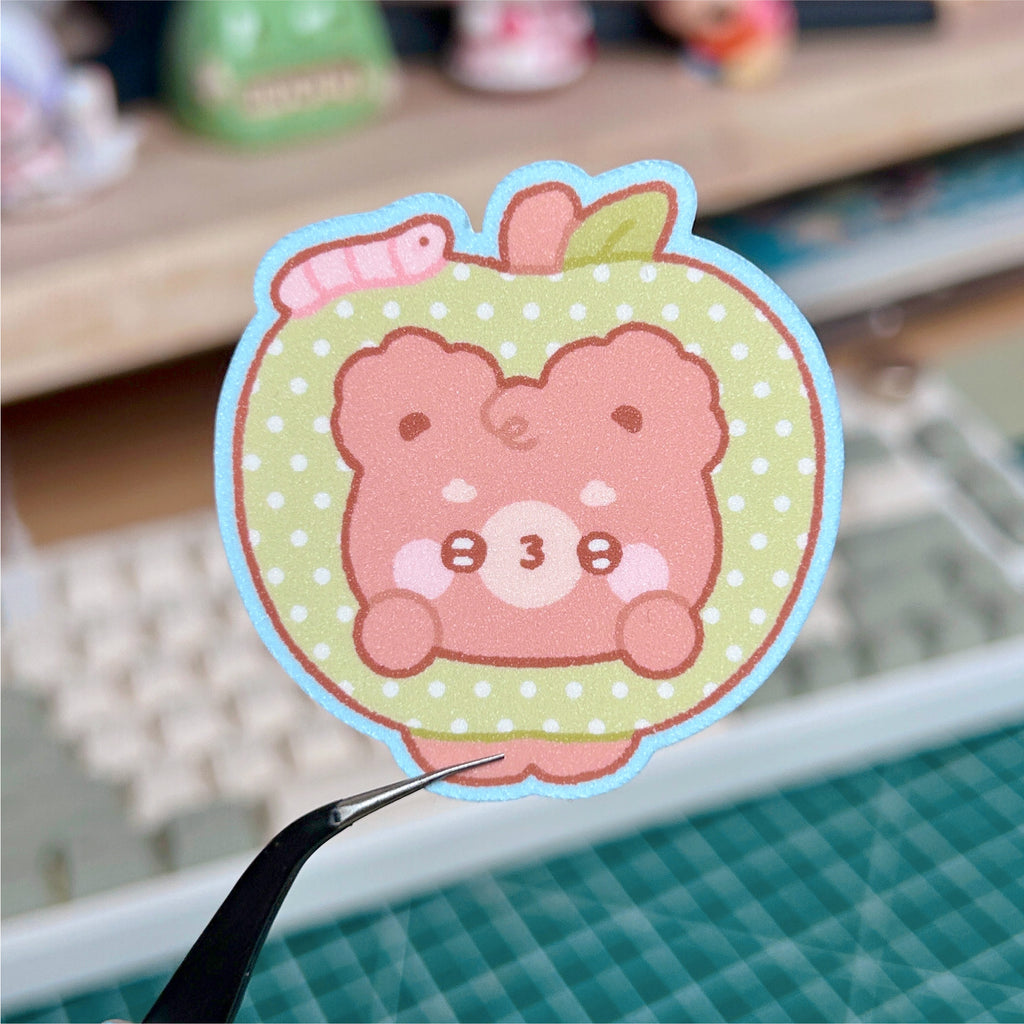 Kawaii bear sticker with a polka dot background held by tweezers on a blurred desk.