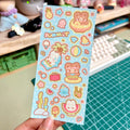 Sheet of colorful stickers with summer-themed designs held over a desk.