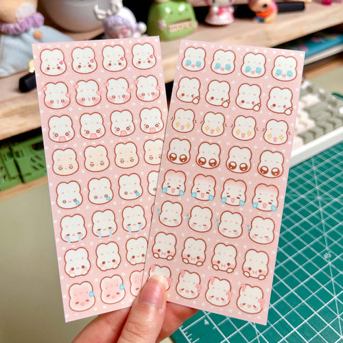 Two sheets of pink bunny stickers held by a hand on a green cutting mat.