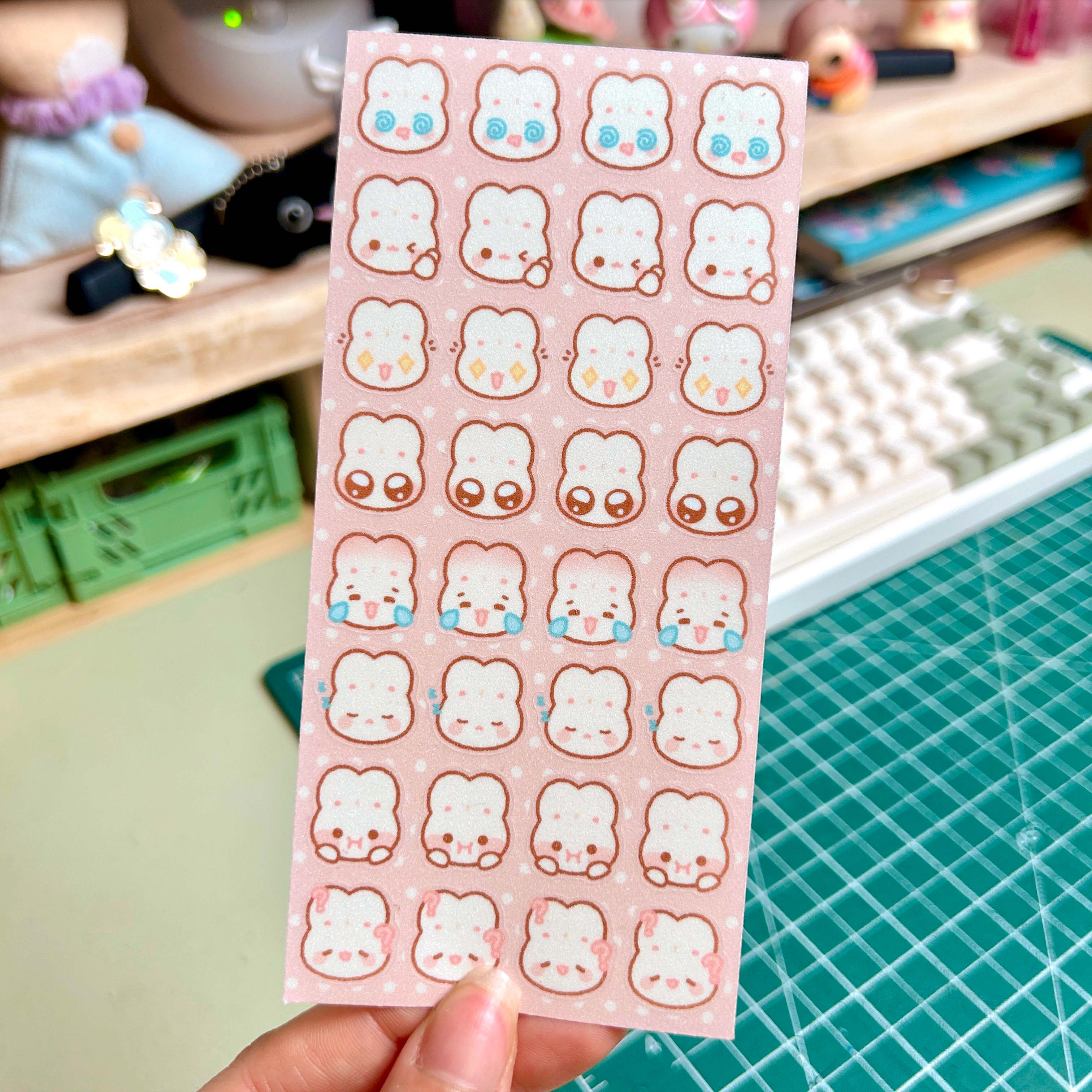 Sheet of cute bunny face stickers held over a crafting table with tools in the background