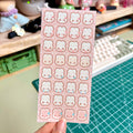 Sheet of cute bunny face stickers held over a desk with stationery items.