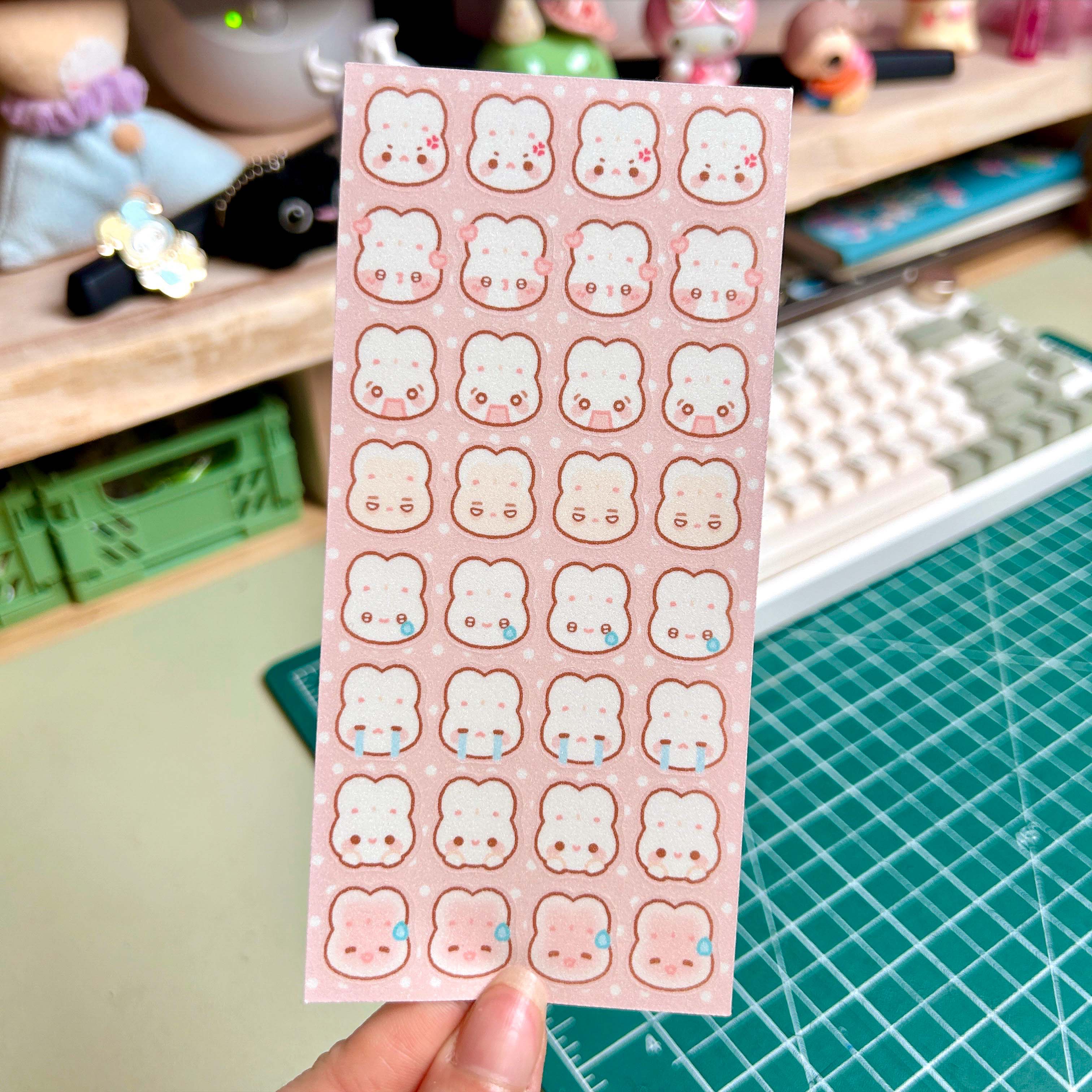 Sheet of cute bunny face stickers held over a desk with stationery items.