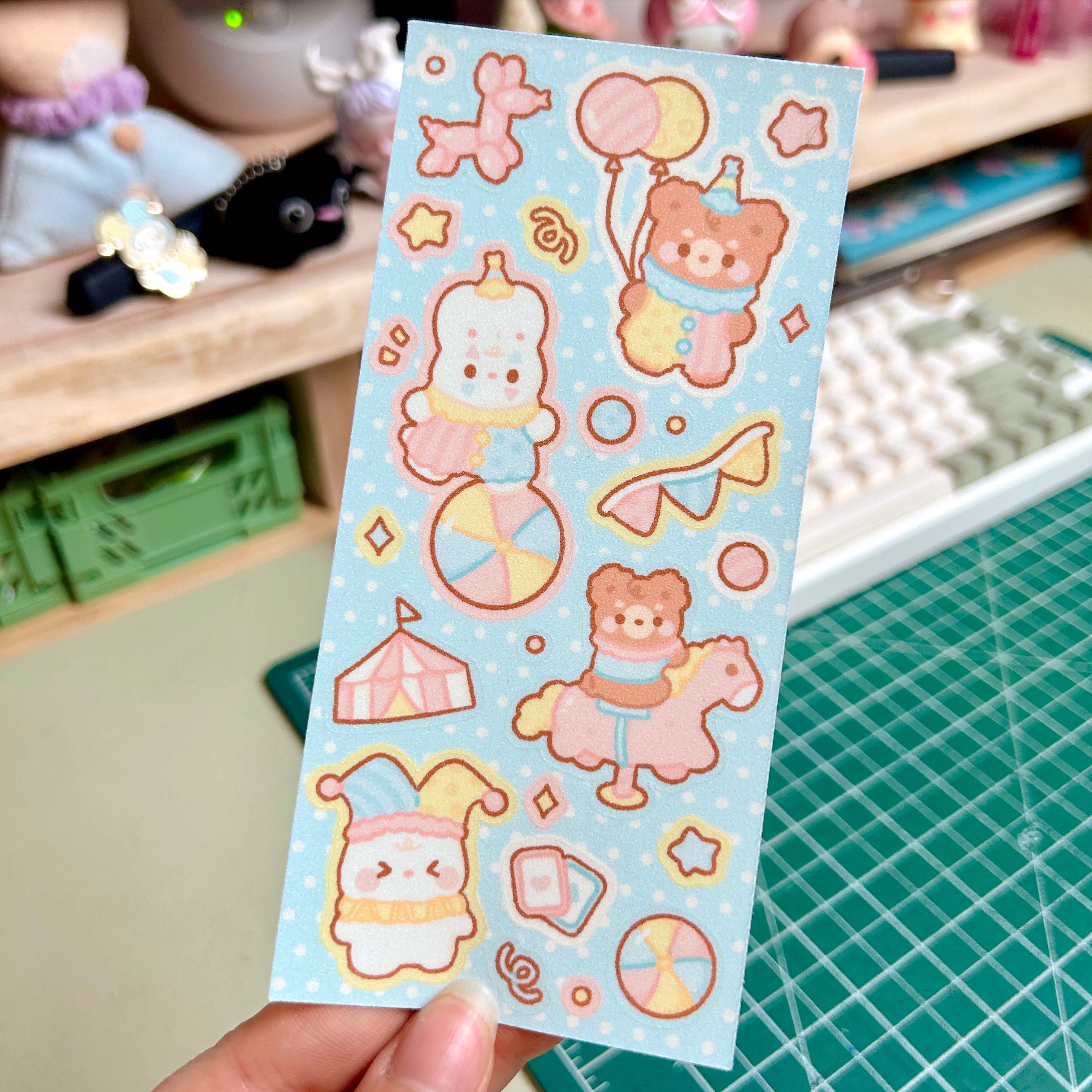 Sheet of cute cartoon stickers held by a hand on a desk with stationery items.