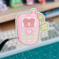 Pink cartoon phone sticker with a teddy bear on a cutting mat.