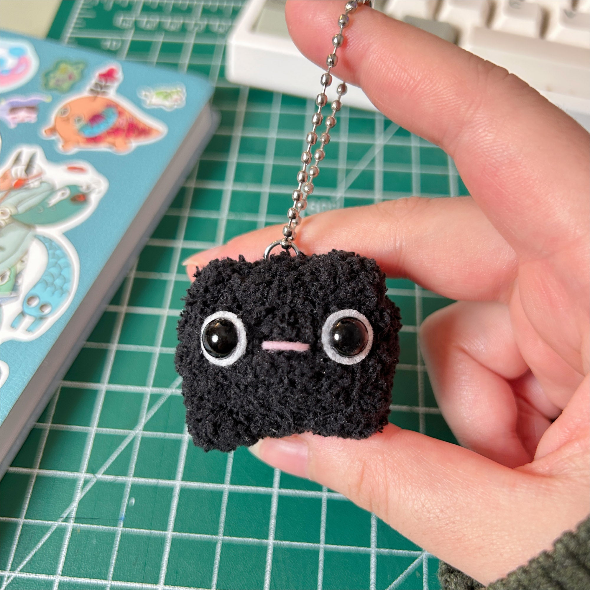 Black crochet keychain held by a hand on a green cutting mat.