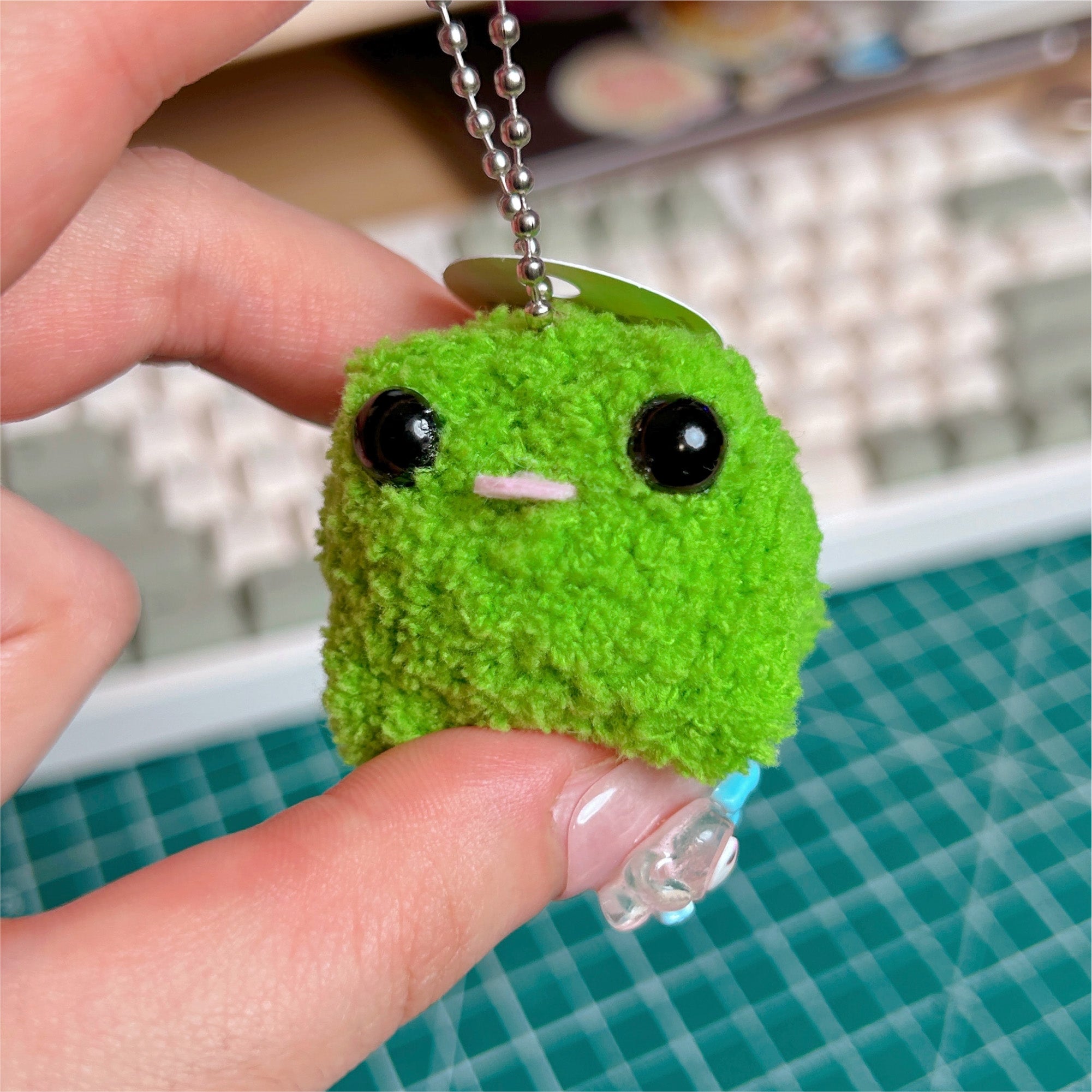 Green plush keychain held by a hand on a blurred background