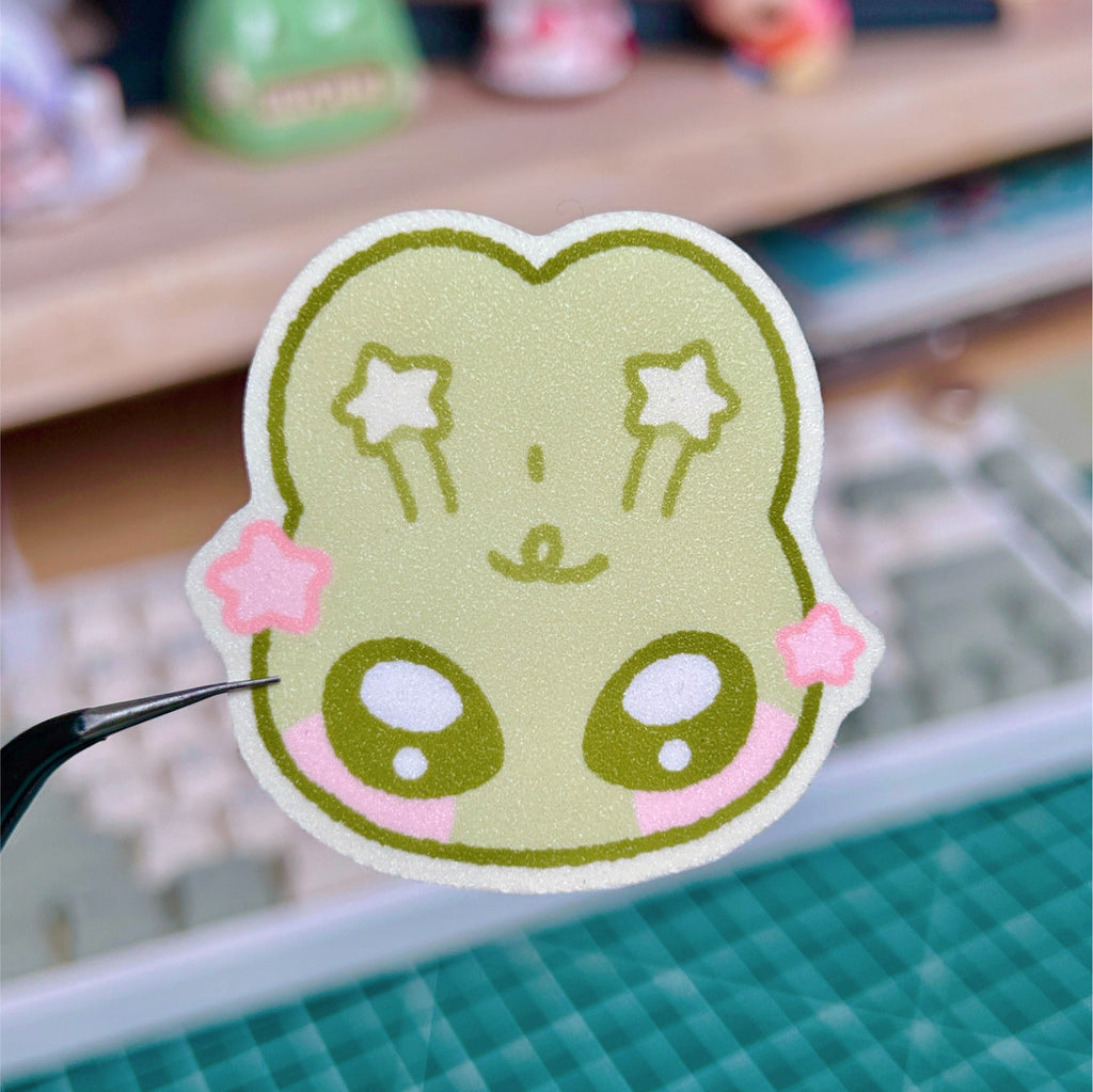 Kawaii-style alien bunny sticker with green and pink accents on a blurred background
