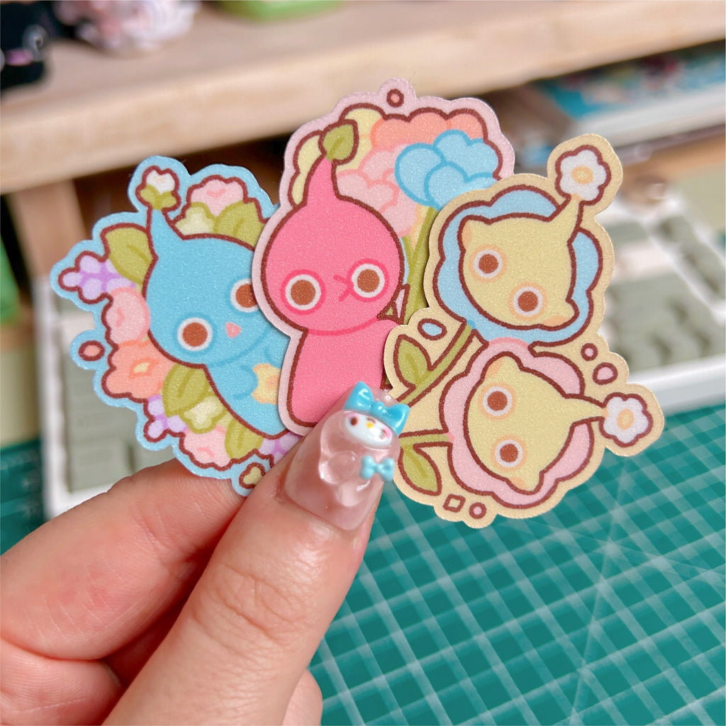Three colorful cartoon stickers held by a hand on a green cutting mat.