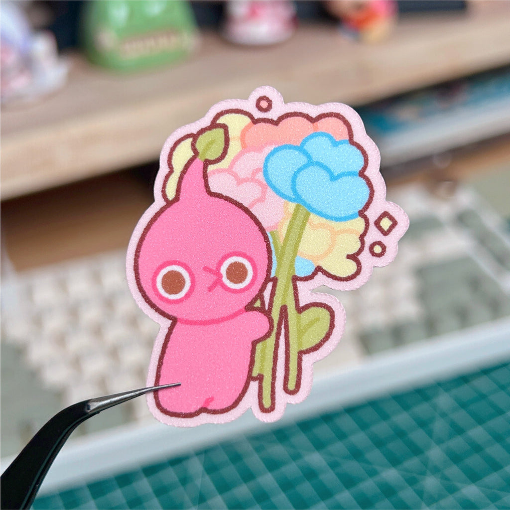 Red cartoon character holding a blue flower on a desk with a keyboard in the background