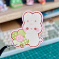 Kawaii-style character sticker held by tweezers on a cutting mat