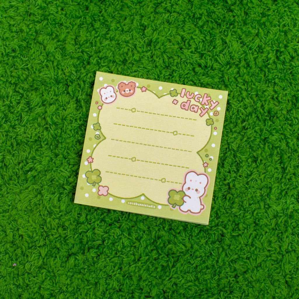 Green notepad with cute character designs and 'lucky day' text on a green textured surface