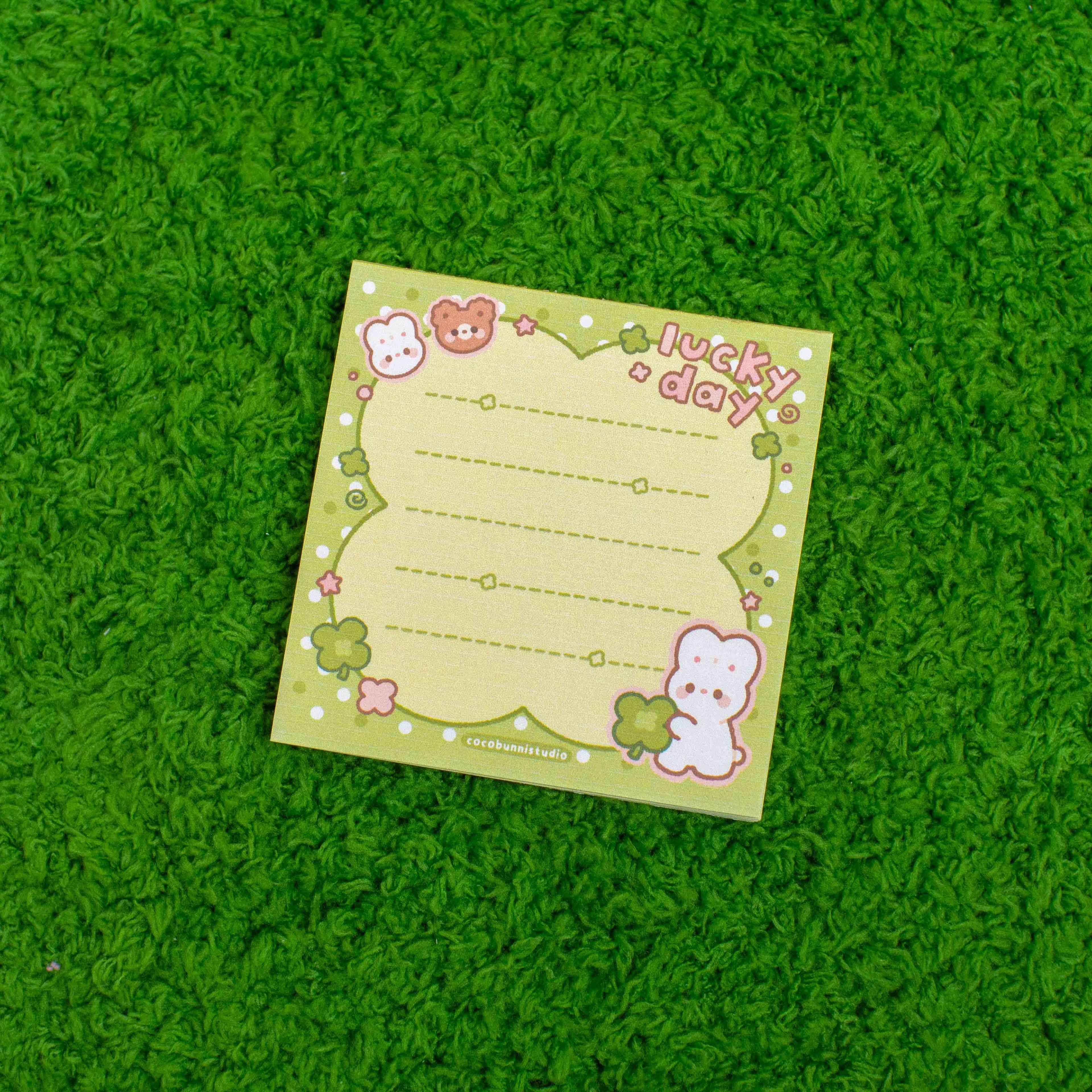 Green notepad with cute character designs and 'lucky day' text on a green textured surface