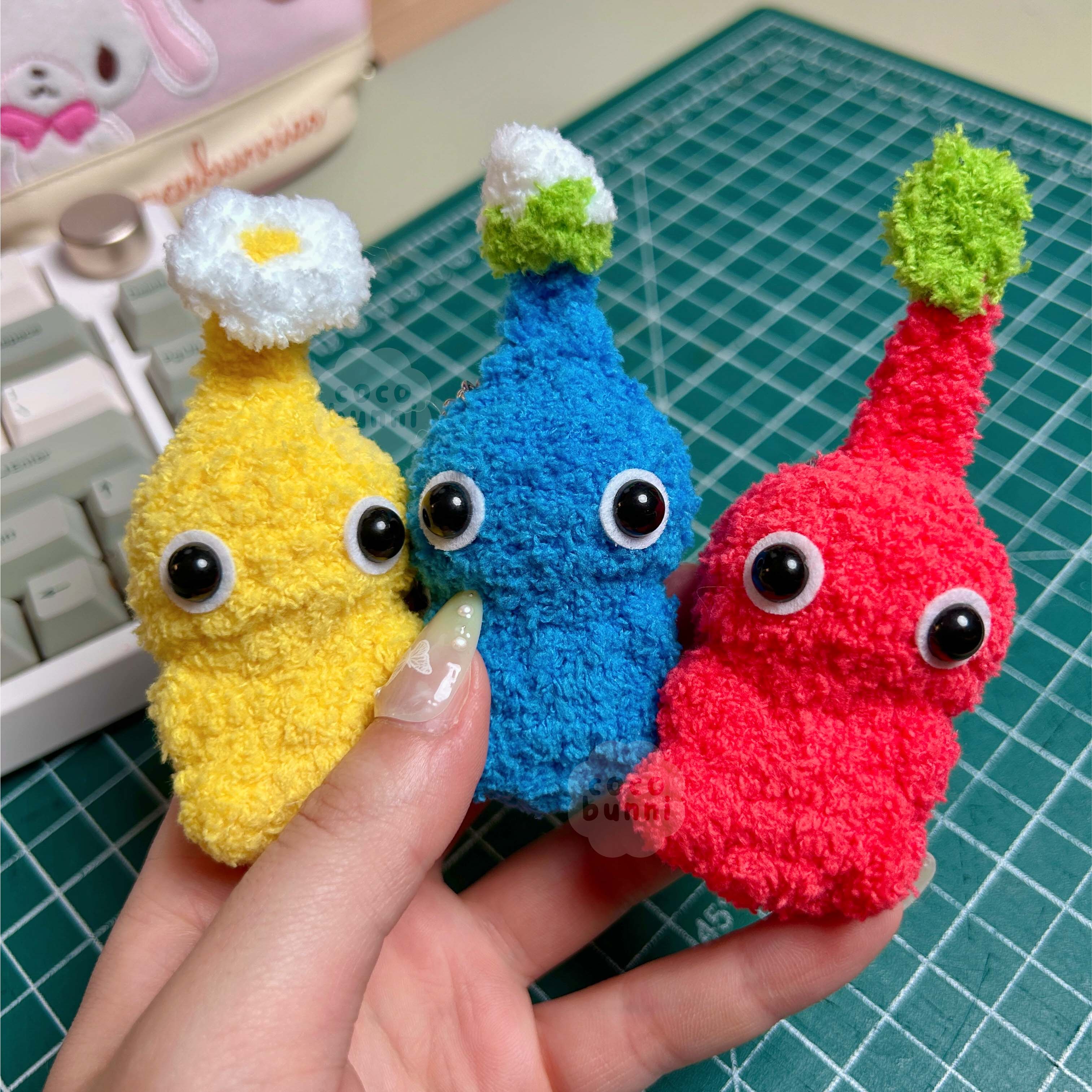 Three colorful plush toys held by a hand on a green cutting mat.