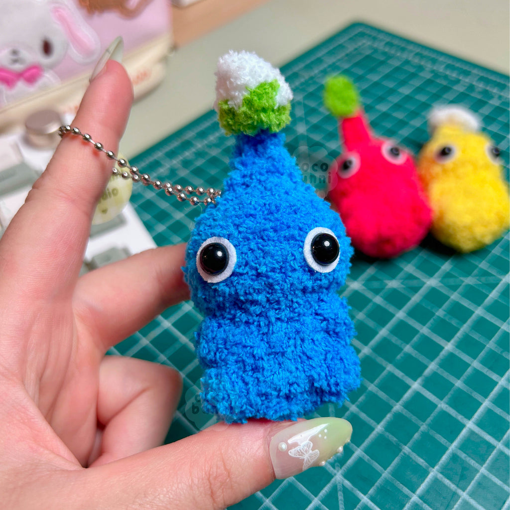 Blue plush keychain held by a hand on a green cutting mat.