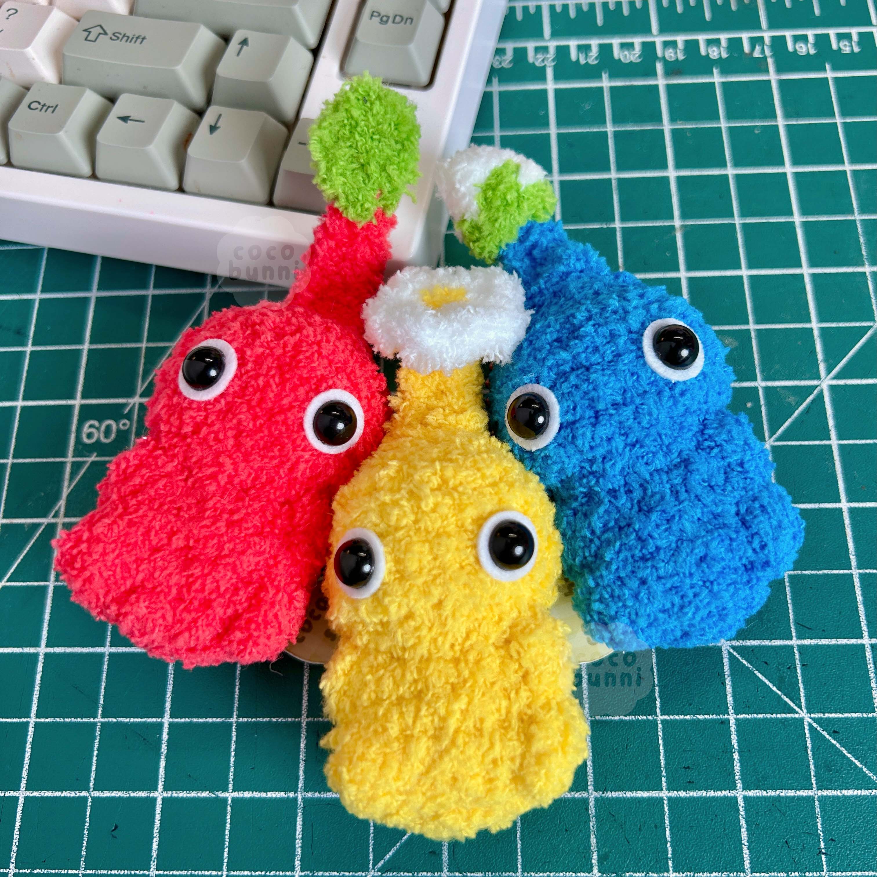 Three colorful plush toys on a green cutting mat with a keyboard in the background.