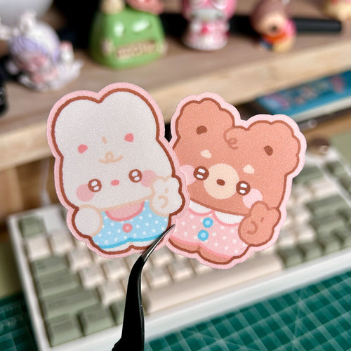 Two cute cartoon character stickers on a desk with stationery items in the background.