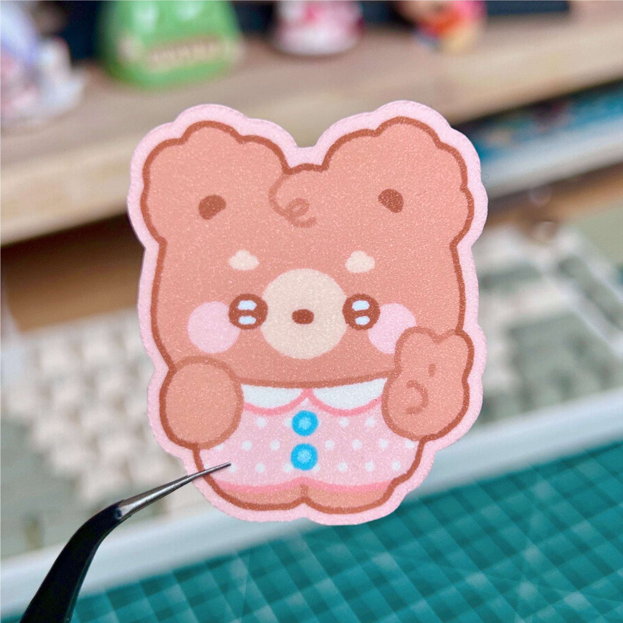 Cartoon bear sticker held by tweezers on a blurred background