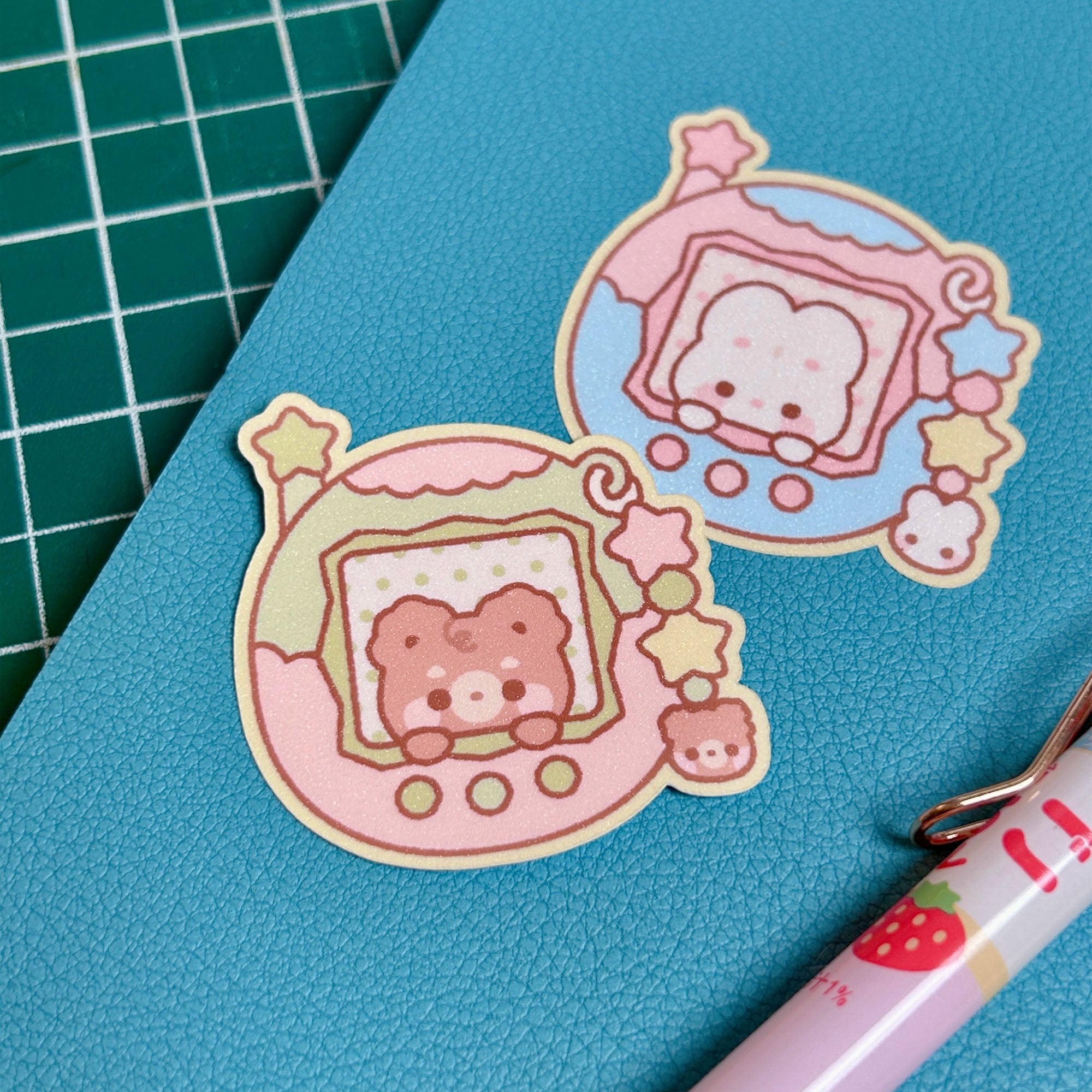 Two cute animal-themed stickers on a blue surface with a pen next to them.