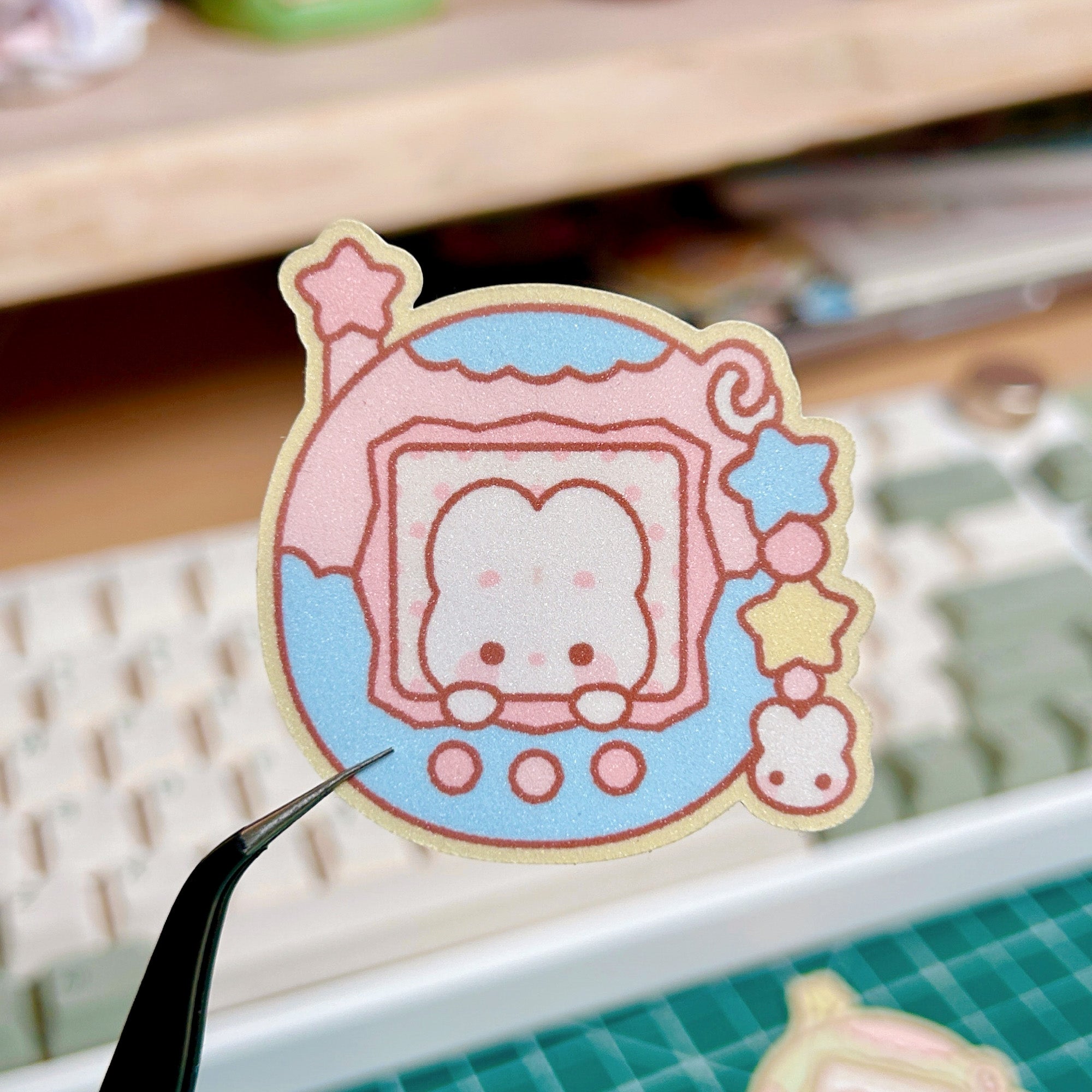 Cartoon cat sticker held by tweezers with a keyboard in the background